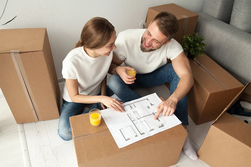 A couple sitting among moving boxes, studying the floor plan of a home