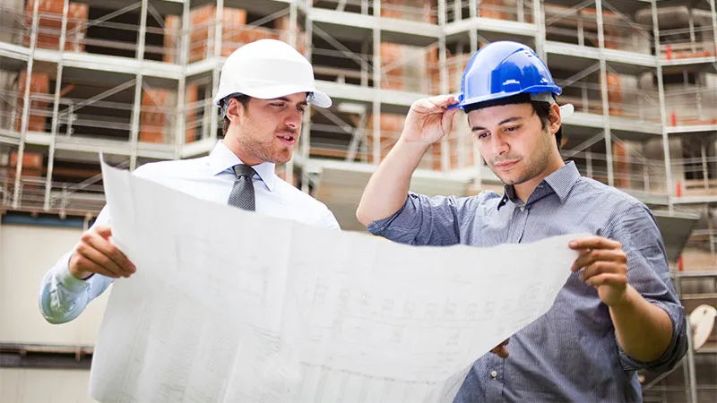 Two builders in hard hats reviewing a building plan on a construction site